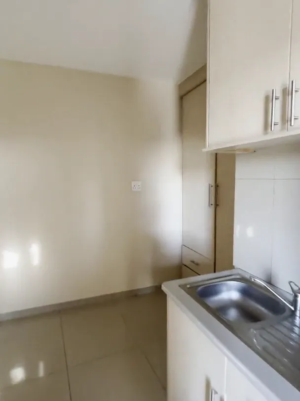 Kitchenette corner with a stainless steel sink, white cupboards above and below, and a tiled floor