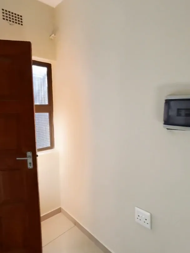 Cream wall with a wall socket and a small electrical box, beside an open wooden door and a small window