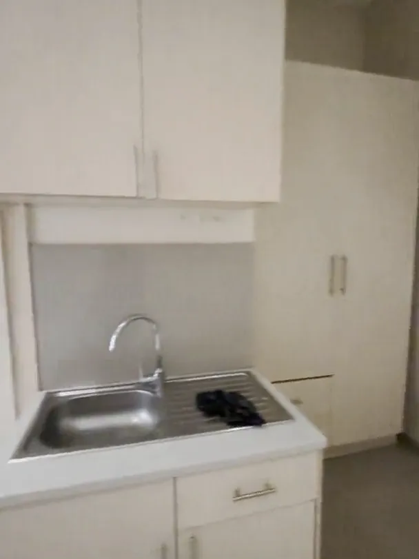 Kitchenette with a stainless steel sink and tap, white cupboards above and below, and a tiled splashback